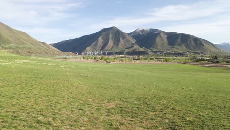 aerial flyover green rural fields showing eco friendly wind turbine farm and wasatch mountains in background