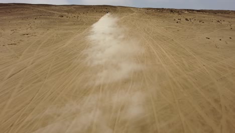 motociclista montando rápidamente una empinada colina del desierto soplando arena en el aire
