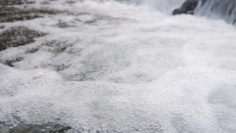 a detailed view of bubbling water in a flowing stream near a waterfall, captured in slow motion for a dynamic effect.