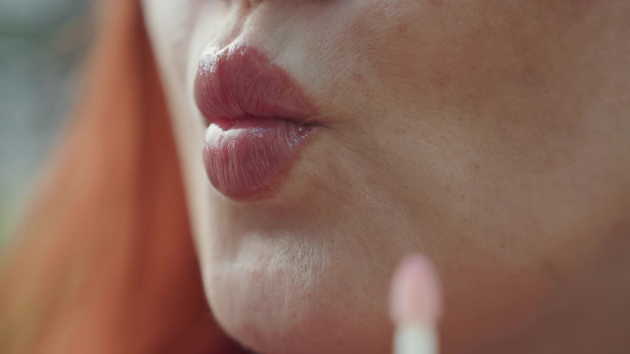 Primo piano di una donna che applica lucidalabbra sulle labbra con mano ferma e applicatore. Le labbra sono mostrate in dettaglio mentre il prodotto viene spalmato uniformemente, evidenziando il cambiamento di texture da secco.