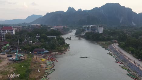 Luftflug-über-Den-Fluss-Nam-Song-Bei-Vang-Vieng-Mit-Festgemachten-Langbooten-Und-Einem-Großen-Bodenkran,-Der-In-Der-Nähe-Geparkt-Ist