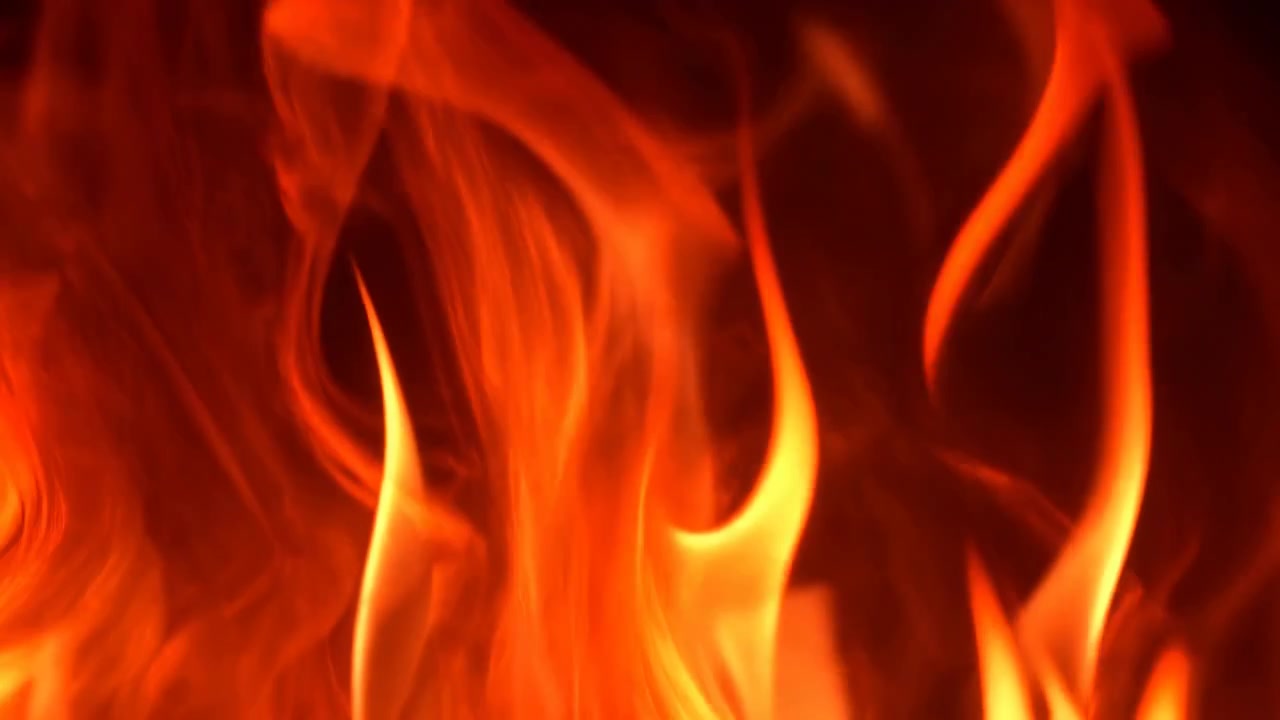 Voldsomme orange flammer på mørk baggrund, nærbillede filmisk loop af dansende ild, intens varme med glød