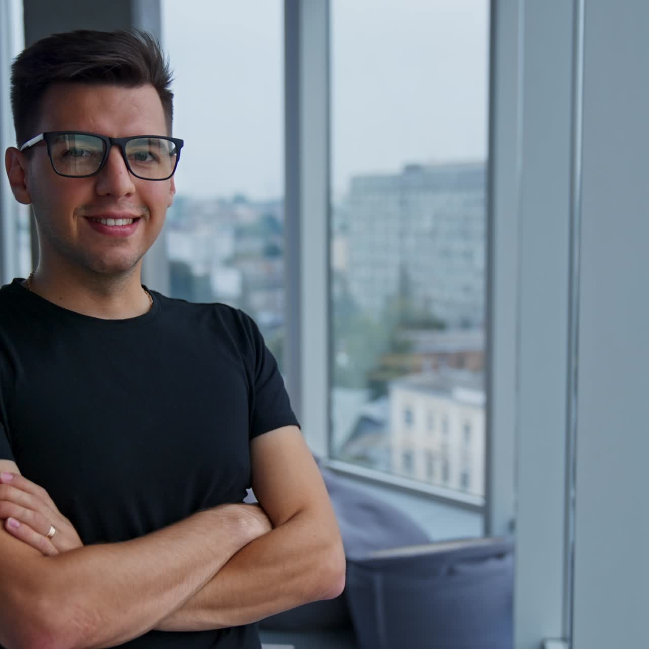 Smiling confident young businessman in the light office. Man puts on glasses looking into camera. Blurred backdrop