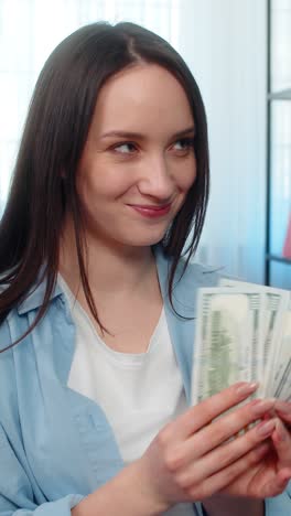 young woman happily counting pile of cash dollar bills on sofa celebrating wealth successful finance