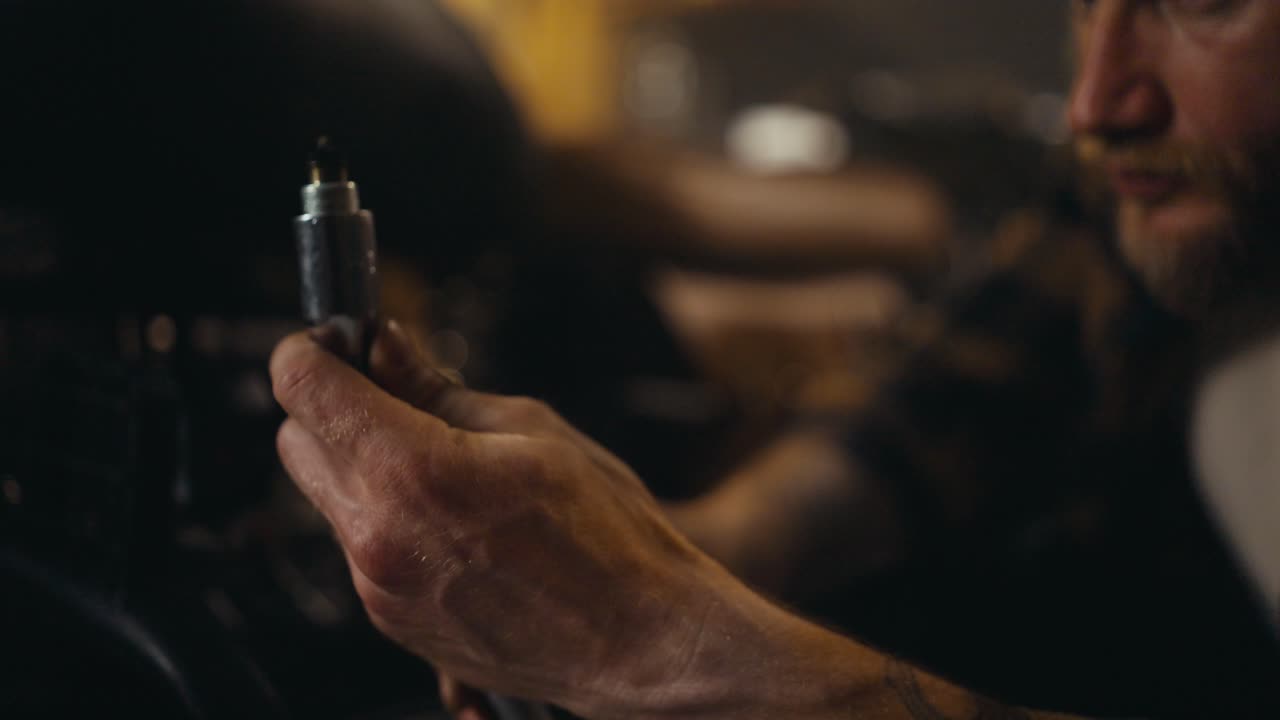 Close-up of a guy mechanic inspecting a spark plug while repairing a motorcycle and picking up tools in his workshop studio