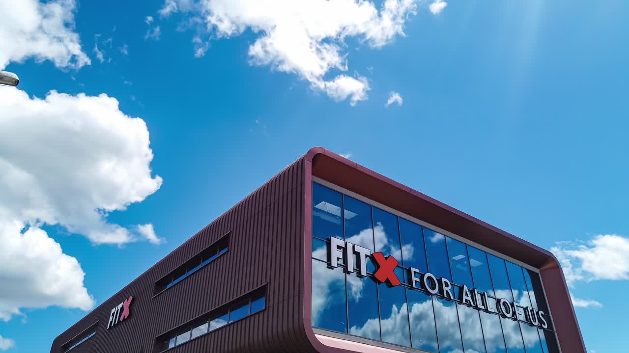 Motion time lapse of modern Fitness studio building with clouds reflection moving across sunny blue sky