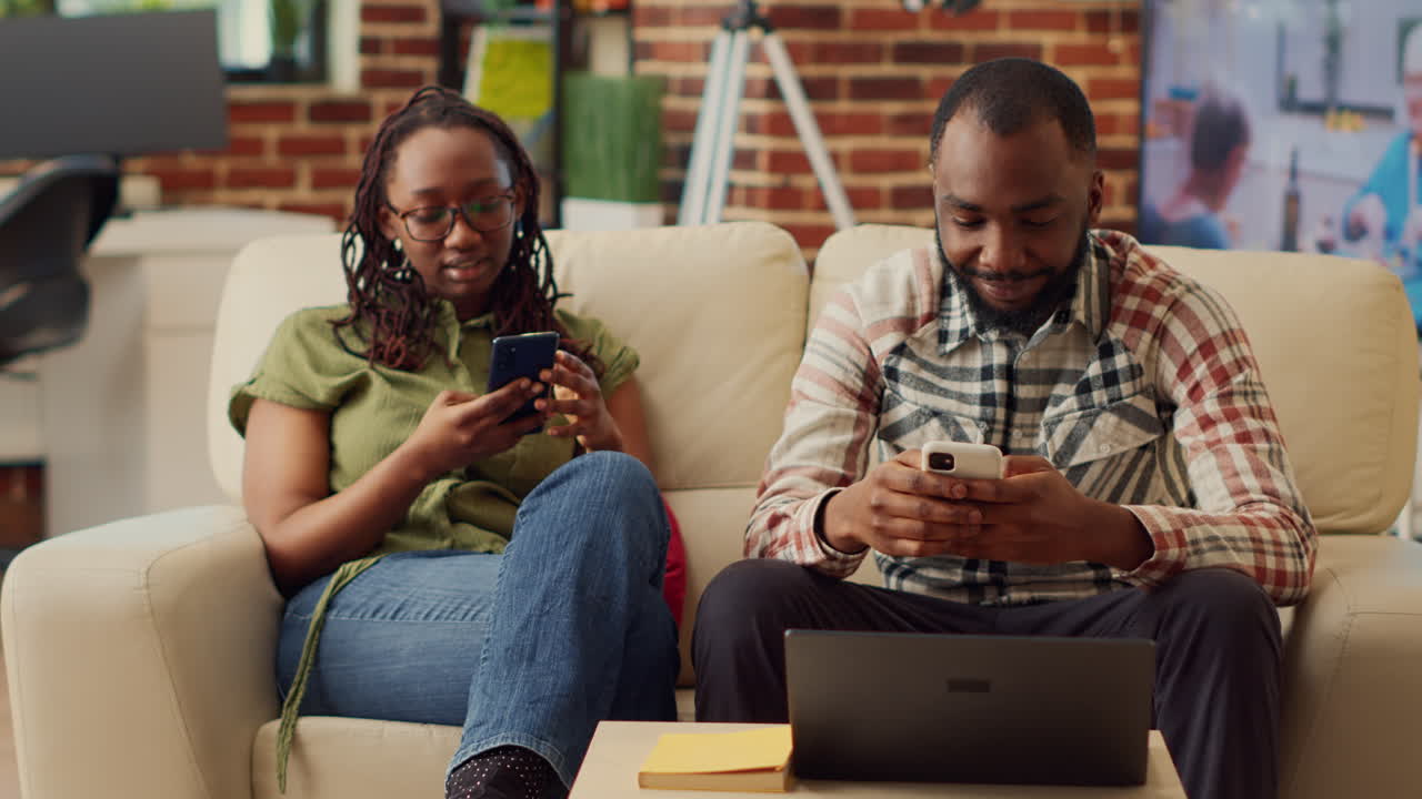 African american couple using smartphones together on sofa