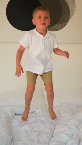 niño se para en la cama con ropa blanca como la nieve preparándose para saltar en el dormitorio de un apartamento moderno. momentos de la infancia positiva. alegría del movimiento activo