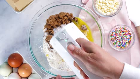 baking confetti sugar cookies and using a white electric mixer to combine the batter. in the kitchen making a dessert. making confetti sugar cookies with a white background, pink napkin and eggs