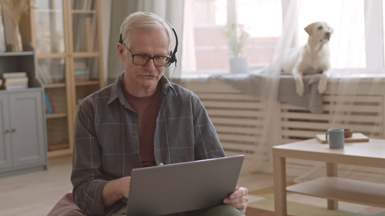 Senior Man with Headset Working on Laptop from Home