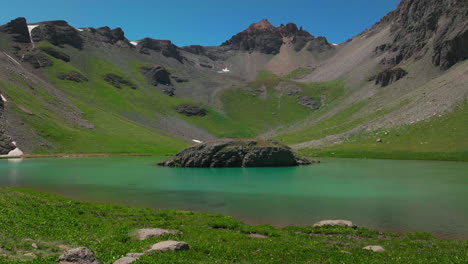 dreamy heavenly island lake silverton ice lake basin aerial drone cinematic unreal caribbean aqua blue silverton colorado lush green wildflower summer snow melting rocky mountains backward movement