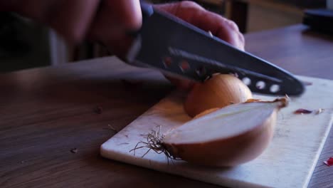 primer plano, cámara en mano, de un anciano cortando algunas cebollas en una tabla de cortar blanca con un cuchillo afilado y las recoge para un plato cajún