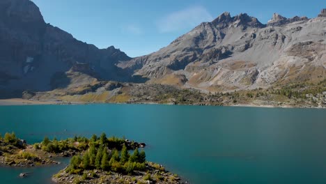 aerial flyover over islands in the waters of lac de salanfe in valais, switzerland on a sunny autumn day in the swiss alps with a pan down view from peaks and cliffs to an overhead view of trees