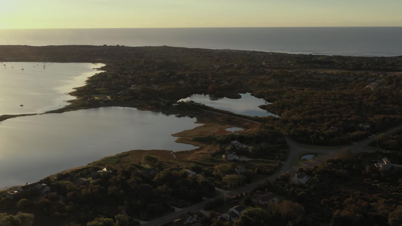 Tomada aérea em movimento sobre o Lago Montauk e o Oceano Atlântico no final de Long Island, Nova York, ao nascer do sol.