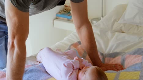 Side-view-of-mid-adult-caucasian-father-leaning-on-bed-and-playing-with-baby-in-comfortable-home-4k