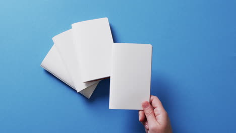 mano sosteniendo un pedazo de papel sobre pedazos de papel con espacio de copia en fondo azul en cámara lenta