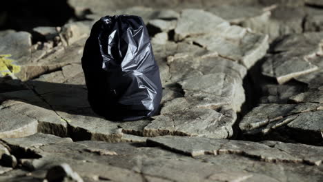 Ein-Schwarzer-Müllsack-Lag-An-Einem-Felsigen-Strand