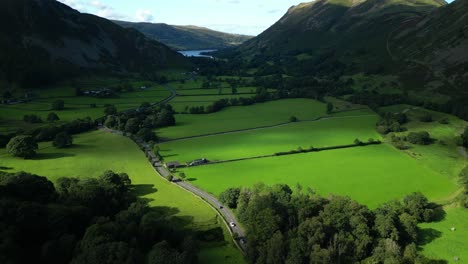 sunlit pools moving across lush green patchwork fields on valley floor with wooded mountainsides and distant lake on summer day