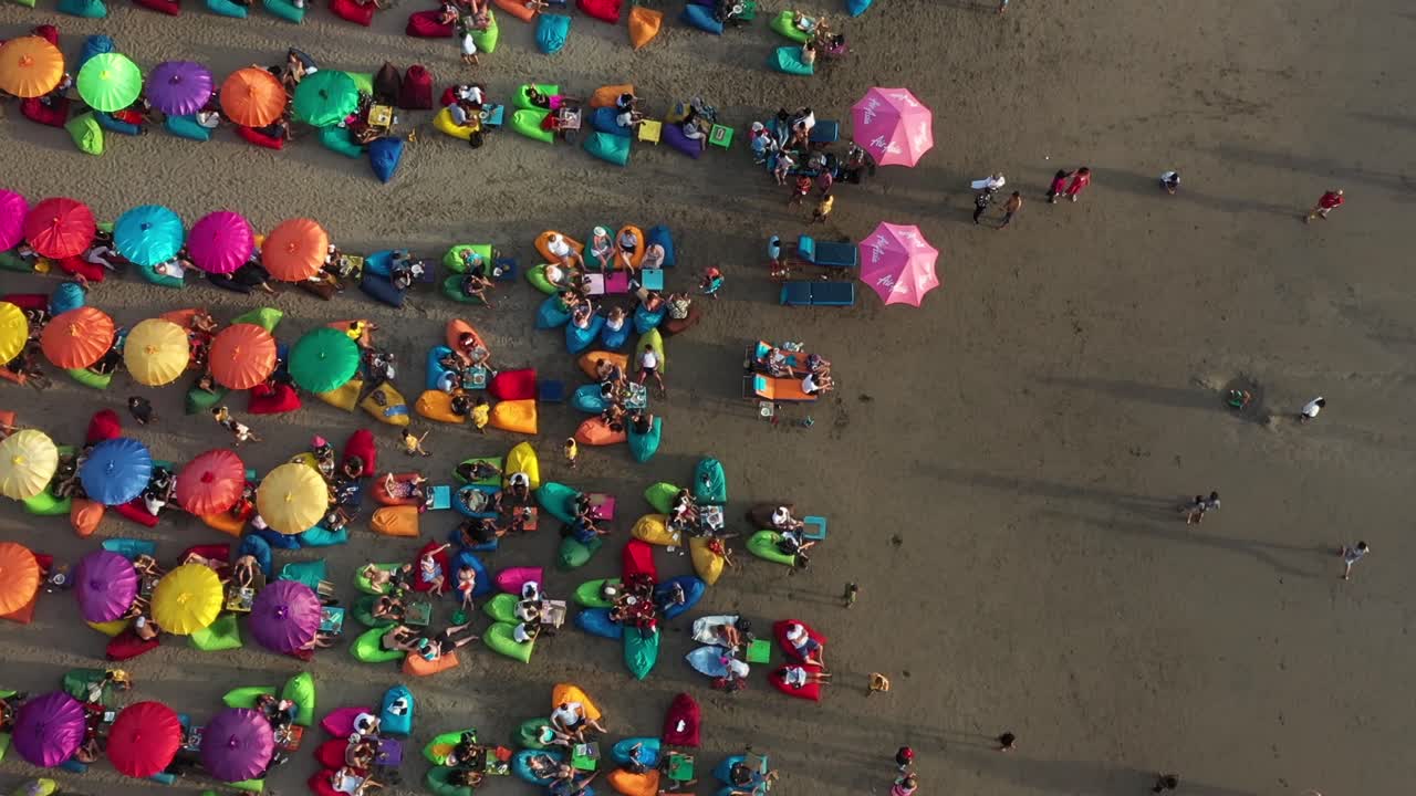 turistas relajándose en las bolsas de frijoles multicolores bajo coloridas sombrillas en la playa de arena tropical