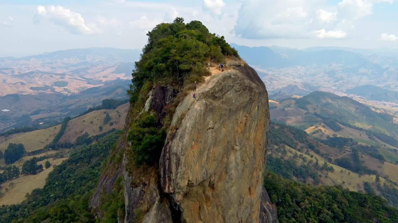 Aerial dolly in on the summit of Pedra Do Bau. A rock climbing team have made a successful ascent to the summit. The zoom in has a Parallax Effect on the surrounding landscape.