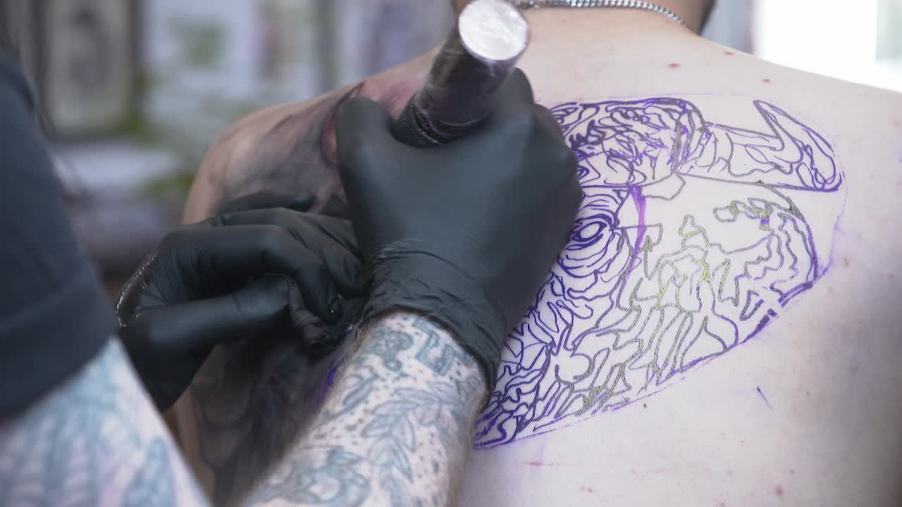 artista del tatuaje tatuando una gran pieza de la espalda con guantes en