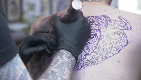 tattoo artist tattooing a big back piece with gloves on