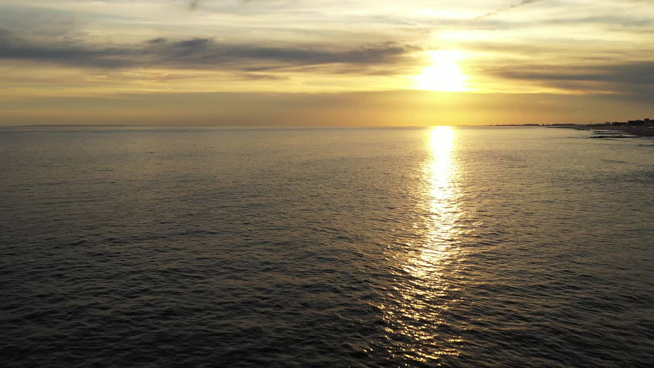 Pull away over surfers in the Atlantic Ocean during a golden sunset then rise up as the camera pulls back