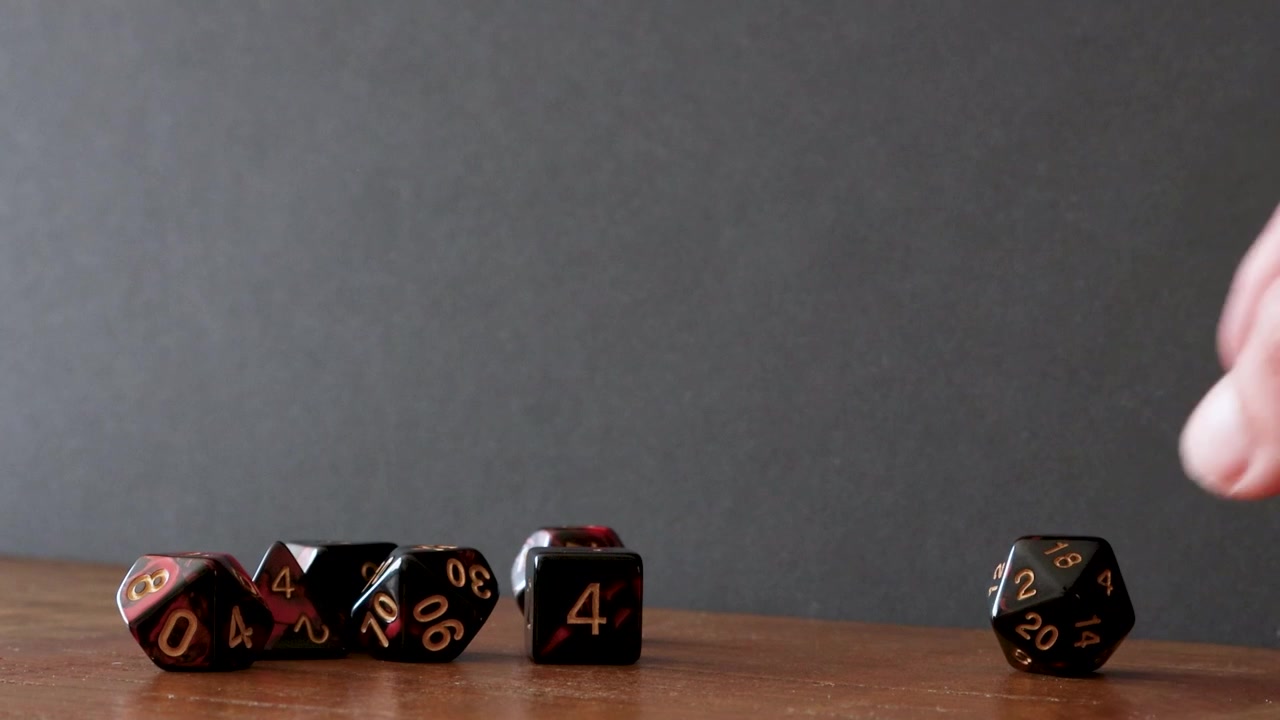 Un mucchio di dadi diversi come un D6, dadi percentili, D4, D10, D12 e D8 giacciono su un tavolo di legno. Un giocatore lancia un D20 nell'inquadratura e dopo pochi secondi lo raccoglie