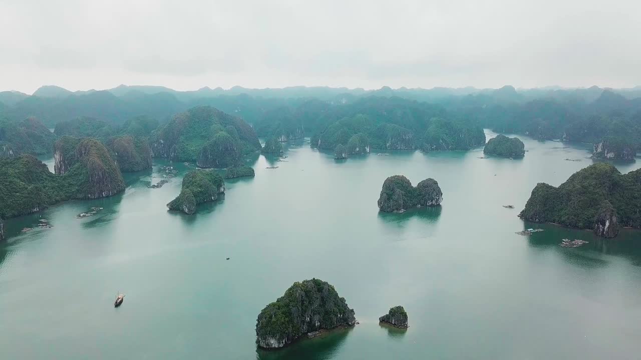 Aerial view of calm bay with limestone islands rising from turquoise water. Lush green cliffs create dramatic natural seascape under cloudy sky, showcasing coastal beauty and peaceful scenery