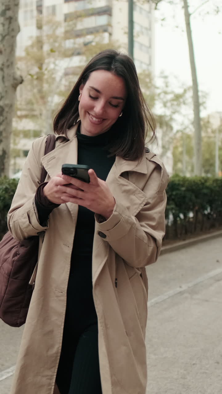 Giovane donna felice che cammina e usa lo smartphone in città