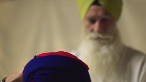 une photo en studio d'un sikh âgé aidant un jeune sikh à attacher du tissu pour un turban sur un fond plat, prise en temps réel.