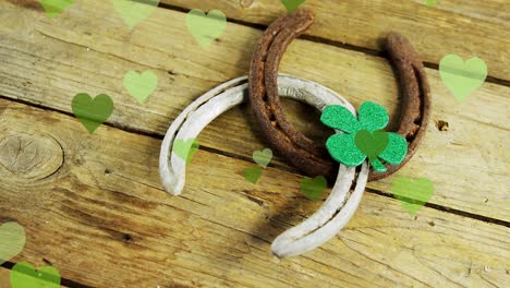 animation of st patrick's shamrock, horseshoe and green hearts on wooden background