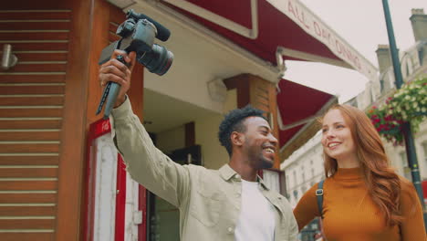 pareja joven viajando por la ciudad juntos vlogging a la cámara de video en trípode de mano