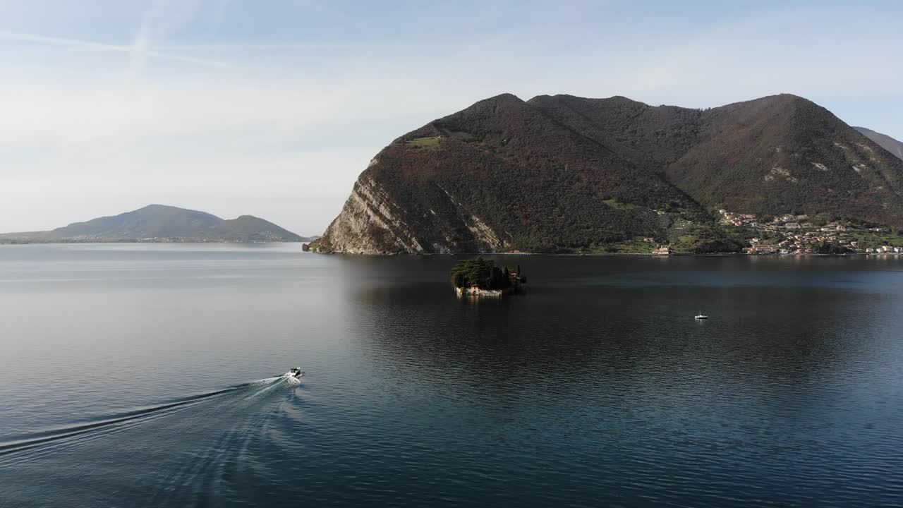 drone follows a boat approaching to San Paolo island on Iseo lake during a sunny autumn day