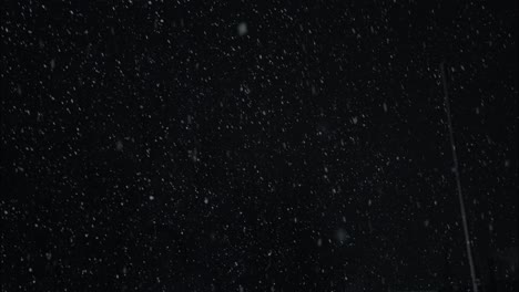 winter snowfall at night snowing on city street in street light