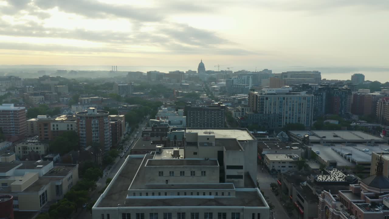 Aerial tracking forward over gloomy city next to lake in soft morning light