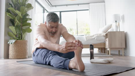 focused senior biracial man practicing yoga stretching at home, slow motion