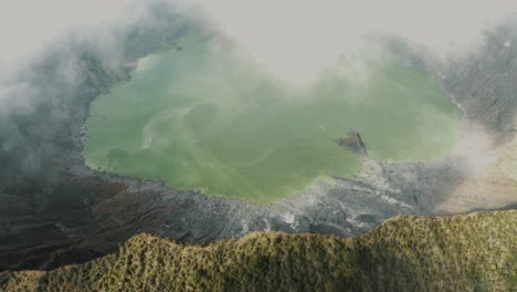 aerial backward movement shot of white clouds blowing across the crater and lake of el chichonal volcano in chiapas, mexico on a cloudy day