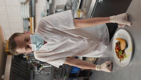 chef in mask serving dish on table
