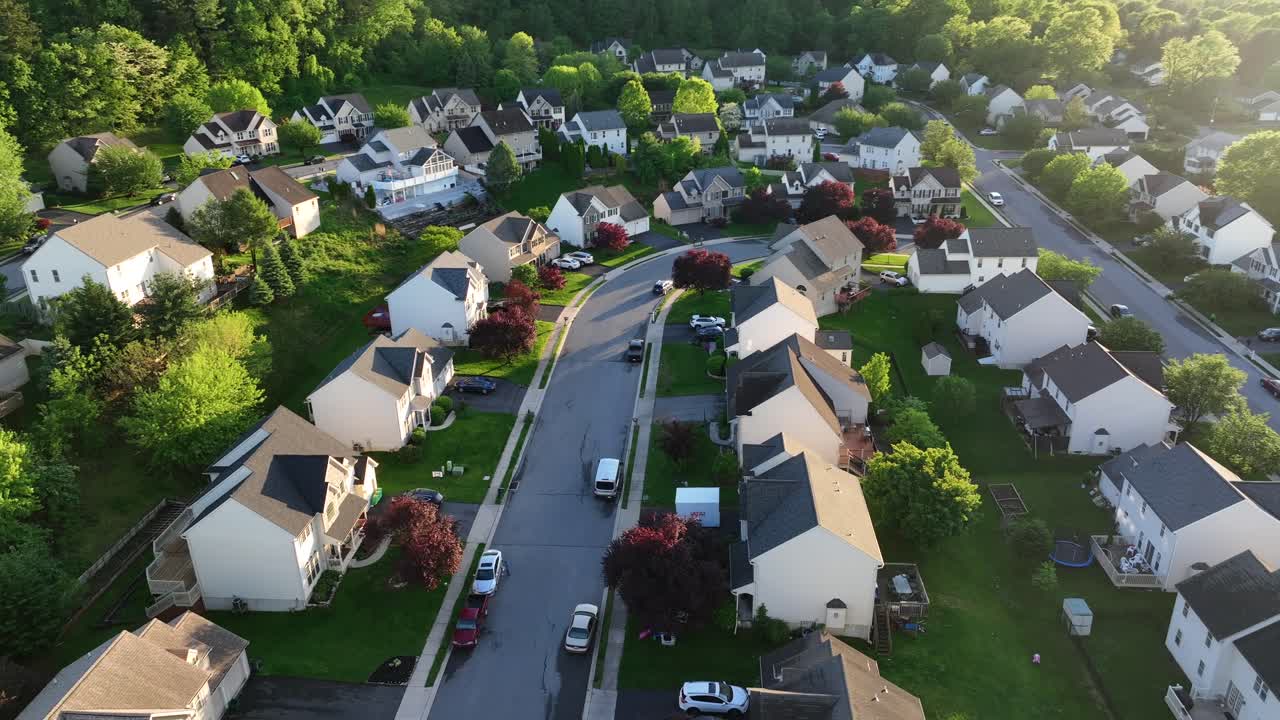 Traditional american housing area with single Family homes at Sunset time in United States. Aerial orbit wide shot. Green forest trees on hills inf Pennsylvania. Blossoming trees in yards.