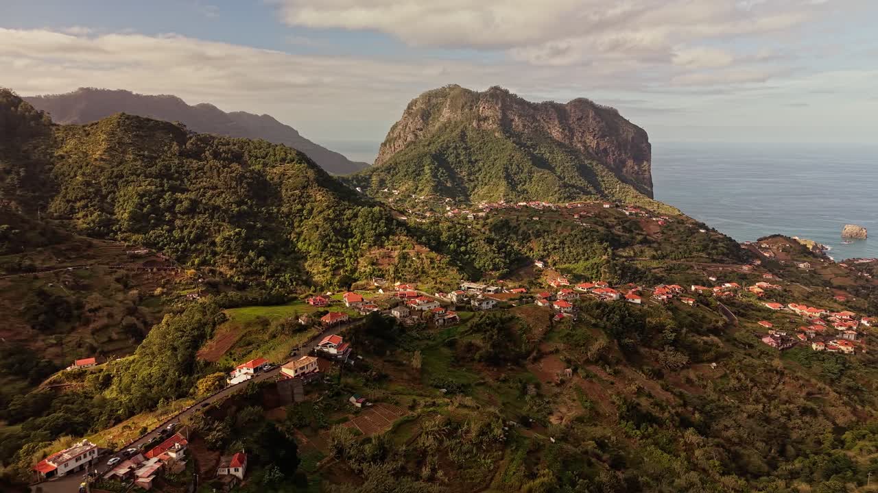 Vista aerea con drone di un villaggio costiero di Madeira incastonato sotto imponenti scogliere rocciose che si affacciano sull'Oceano Atlantico