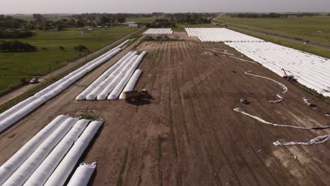 Aerial-drone-view-of-tractor-taking-harvest-from-white-silo-bags-in-farm-of-Buenos-Aires-countryside