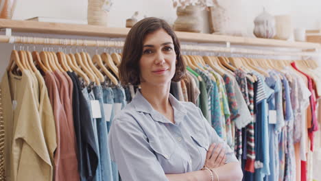 retrato de la propietaria de una tienda de moda de pie frente a la ropa en los rieles