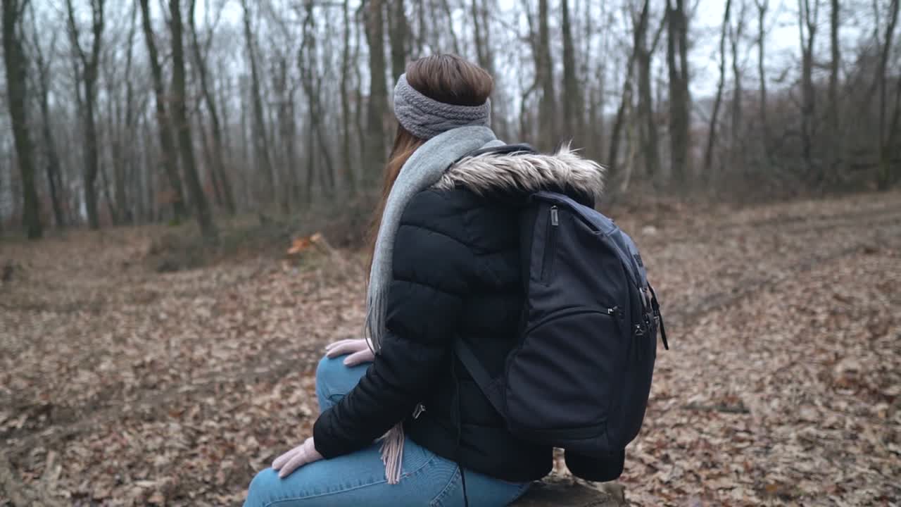 Female caucasian photographer with gray headband and backpack sitting on stump in forest