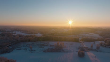 aerial establishing view of a rural landscape in winter, snow covered countryside fields, cold freezing weather, sunset with golden hour light, wide drone shot moving backward