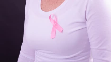 Video-of-midsection-of-caucasian-woman-wearing-pink-cancer-awareness-ribbon,-with-black-background