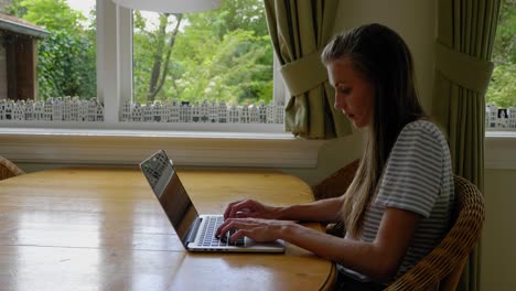 Young-woman-types-on-laptop-at-table-at-home,-pan,-profile,-pan