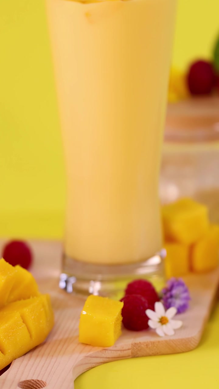 Primo piano luminoso di un dessert smoothie al mango, frutta fresca, panna montata e fiori su sfondo giallo