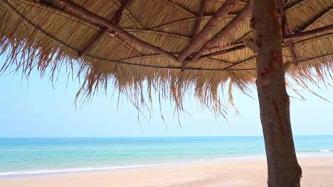 Punto-De-Vista-Desde-Debajo-De-Una-Sombrilla-Tejida-De-Hojas-De-Palma-Mira-Hacia-La-Playa-Hacia-El-Océano