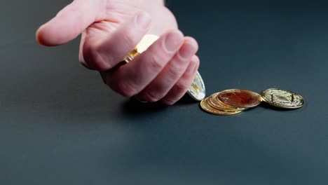 person drops handful of various cryptocurrency coins and mini gold bars onto blue surface, slow motion.